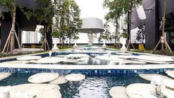 A modern outdoor pool area with circular water features and a central fountain, surrounded by trees and modern architecture.