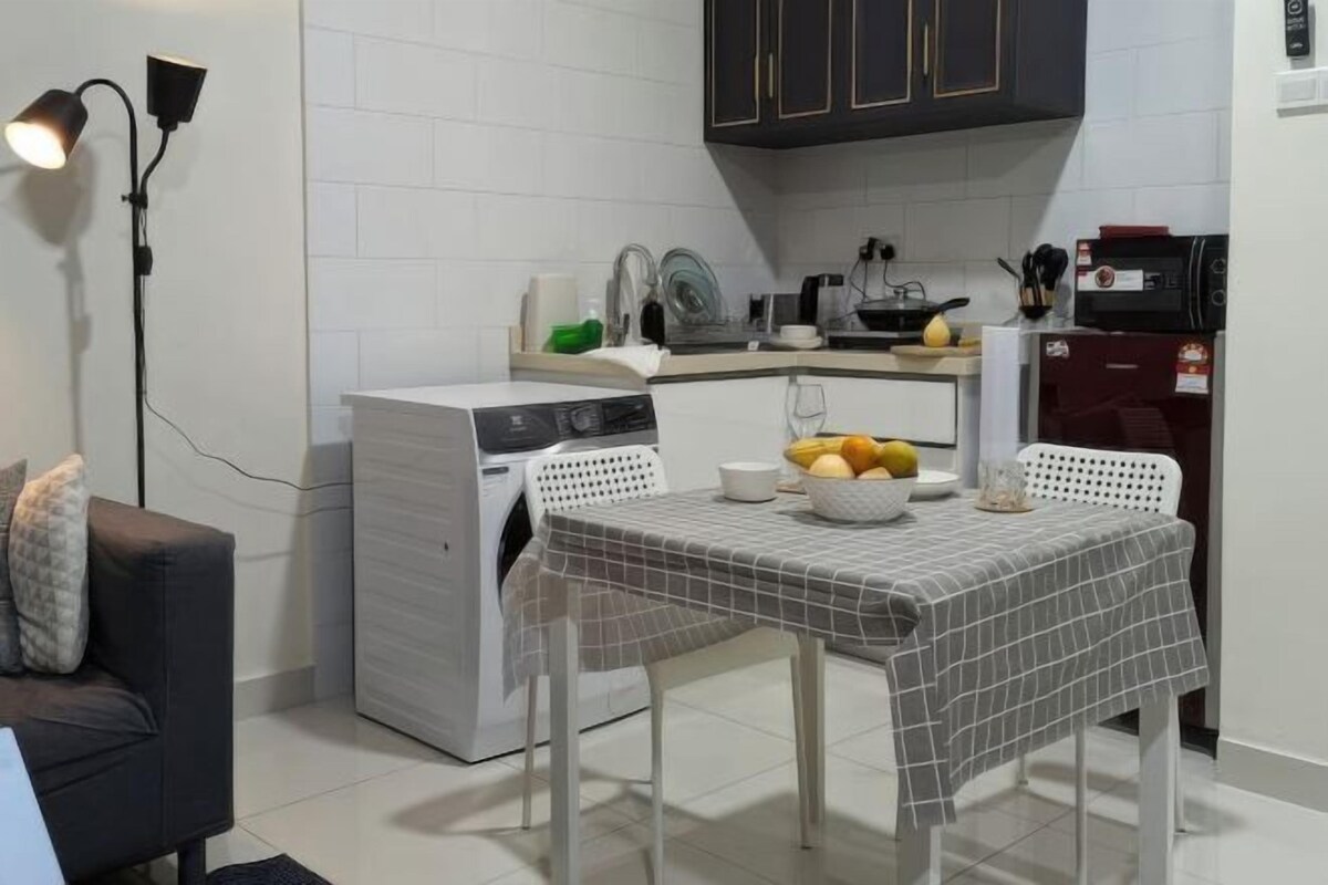 A compact kitchen with a washing machine, a dining table with a checkered tablecloth, and a microwave.