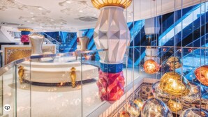 Eine luxuriöse Lobby mit einem runden Tisch in der Mitte, einer Zierpfeiler und einer modernen Treppe mit Glasgeländern.