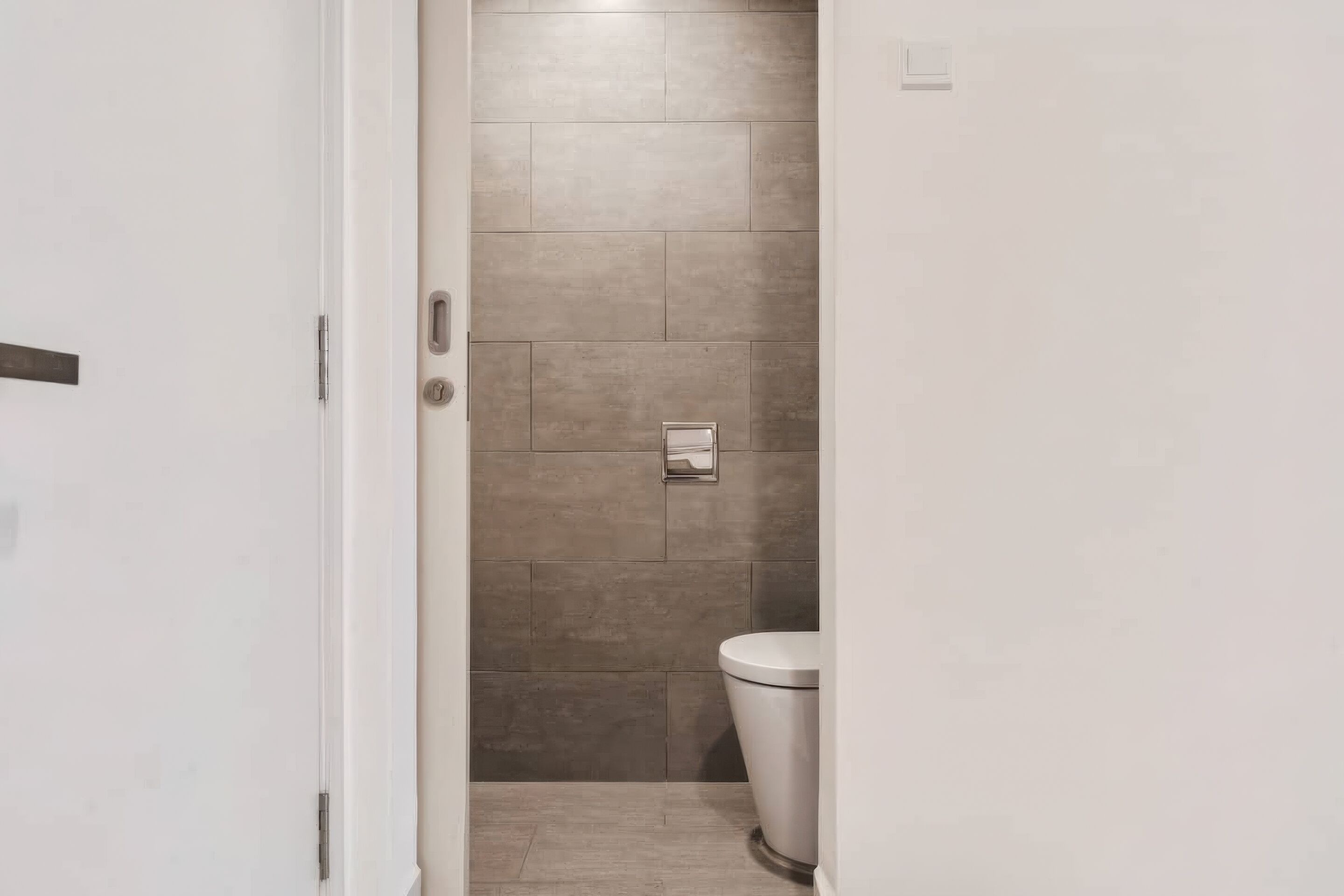 A bathroom with a toilet, a shower area, and a wall-mounted towel dispenser.