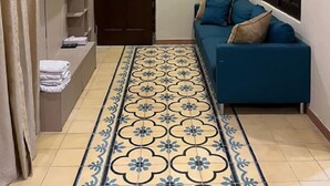 A hallway with a blue sofa, a TV mounted on the wall, a patterned floor, and a door. - Attanaya Malioboro Suites (Yogyakarta)