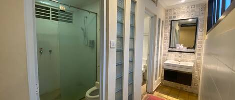 Un bagno con box doccia in vetro, un water, un lavandino con specchio e un cestino.