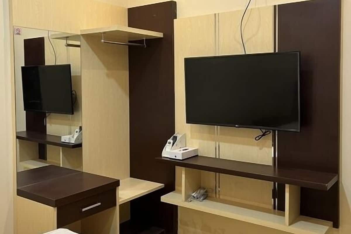 Ein Hotelzimmer mit Bett, Schreibtisch, Wandfernseher und Spiegel über dem Schreibtisch.