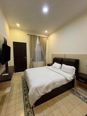 Un dormitorio con cama, televisor, puerta y cortinas.