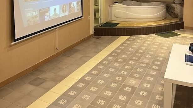 A room with a large screen displaying a streaming service interface, a hot tub, and a patterned floor. - Attanaya Malioboro Suites (Yogyakarta)