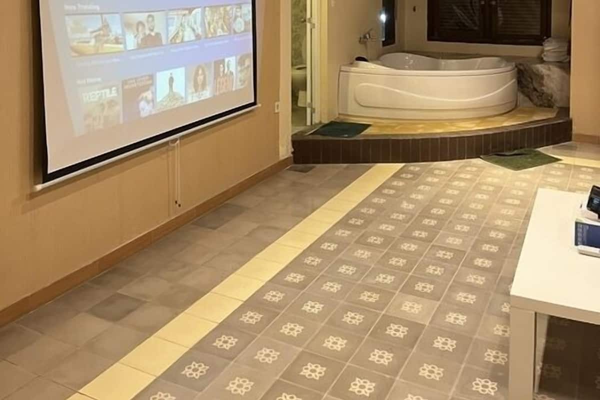 Ein Zimmer mit einem großen Bildschirm, der eine Streaming-Oberfläche zeigt, einer Whirlwanne und einem gemusterten Boden.