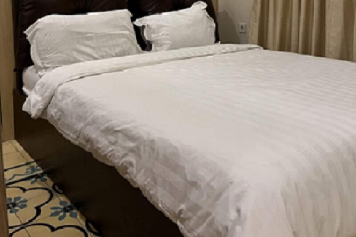 Ein Bett mit Holz-Kopfteil, weißer Bettwäsche und einem gemusterten Boden.