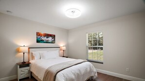 Ein Schlafzimmer mit einem Bett, Nachttischen, einem Fenster und einem Bild an der Wand.
