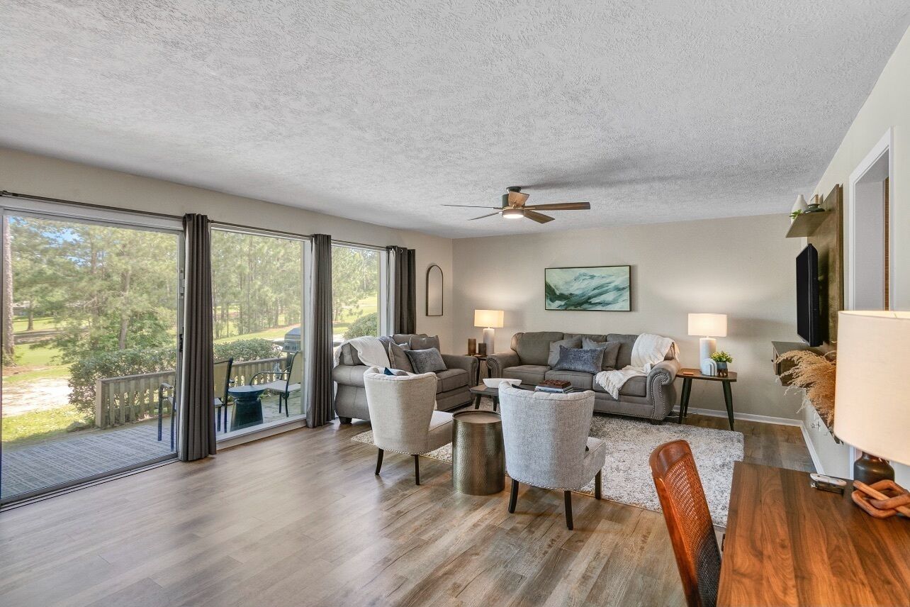 A spacious living room with a large sliding glass door leading to a balcony, a ceiling fan, and a modern fireplace.
