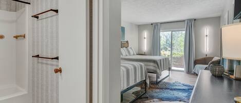 A modern bedroom with a large bed, a desk, and a view of the outdoors.