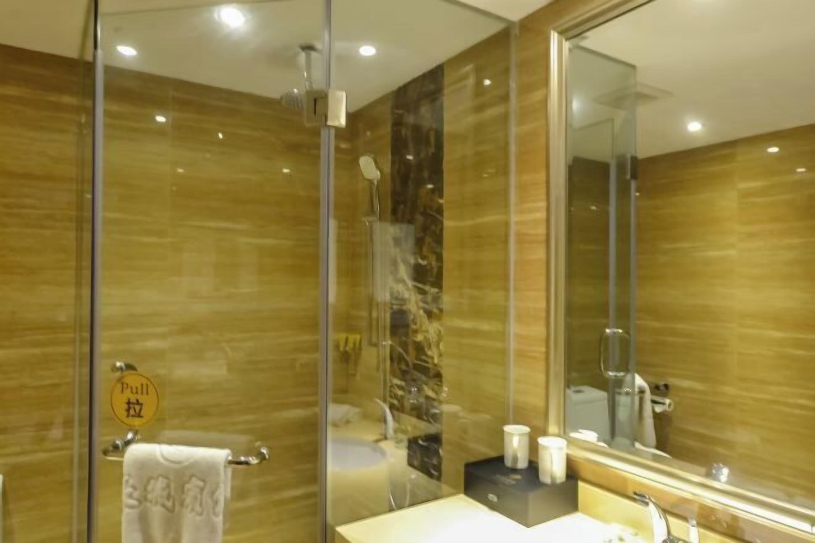 A modern bathroom with a glass shower enclosure, a large mirror, and a towel rack with a 'pull' sign.