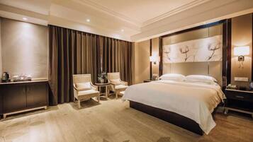 A hotel room with a large bed, two armchairs, a small table, a cabinet, and a decorative wall.