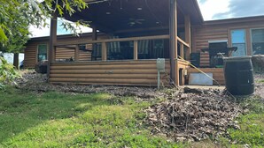 Una cabaña de madera con un porche cubierto, una antena parabólica y una zona de barbacoa.