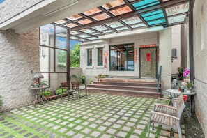 A covered patio with a checkered floor, outdoor seating, and a building entrance with steps.