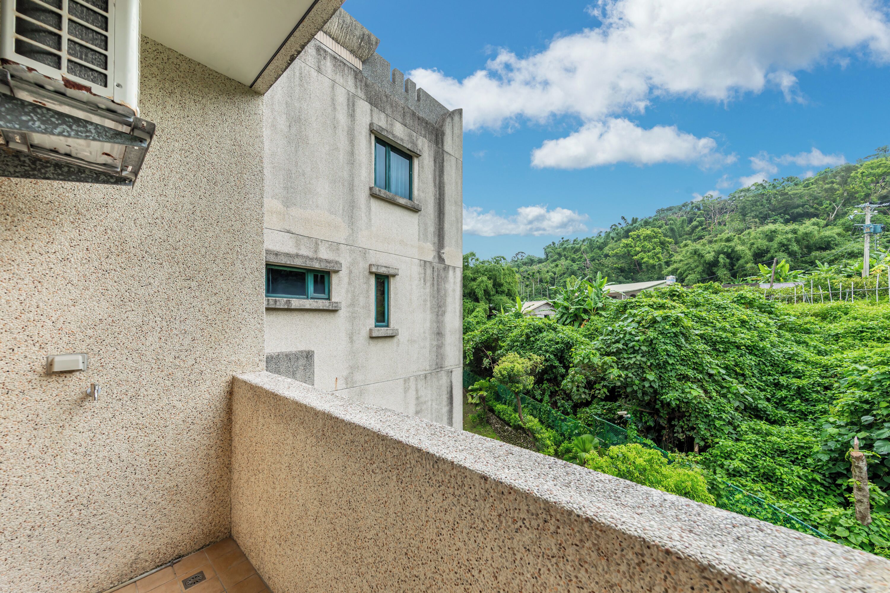 Un balcón con pared de concreto y ventana con vista a una colina verde exuberante.