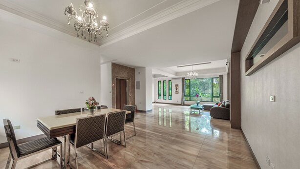 Un vaste espace dédié à la salle à manger, avec une grande table et des chaises, un lustre et une vue sur l’extérieur grâce à de grandes fenêtres.