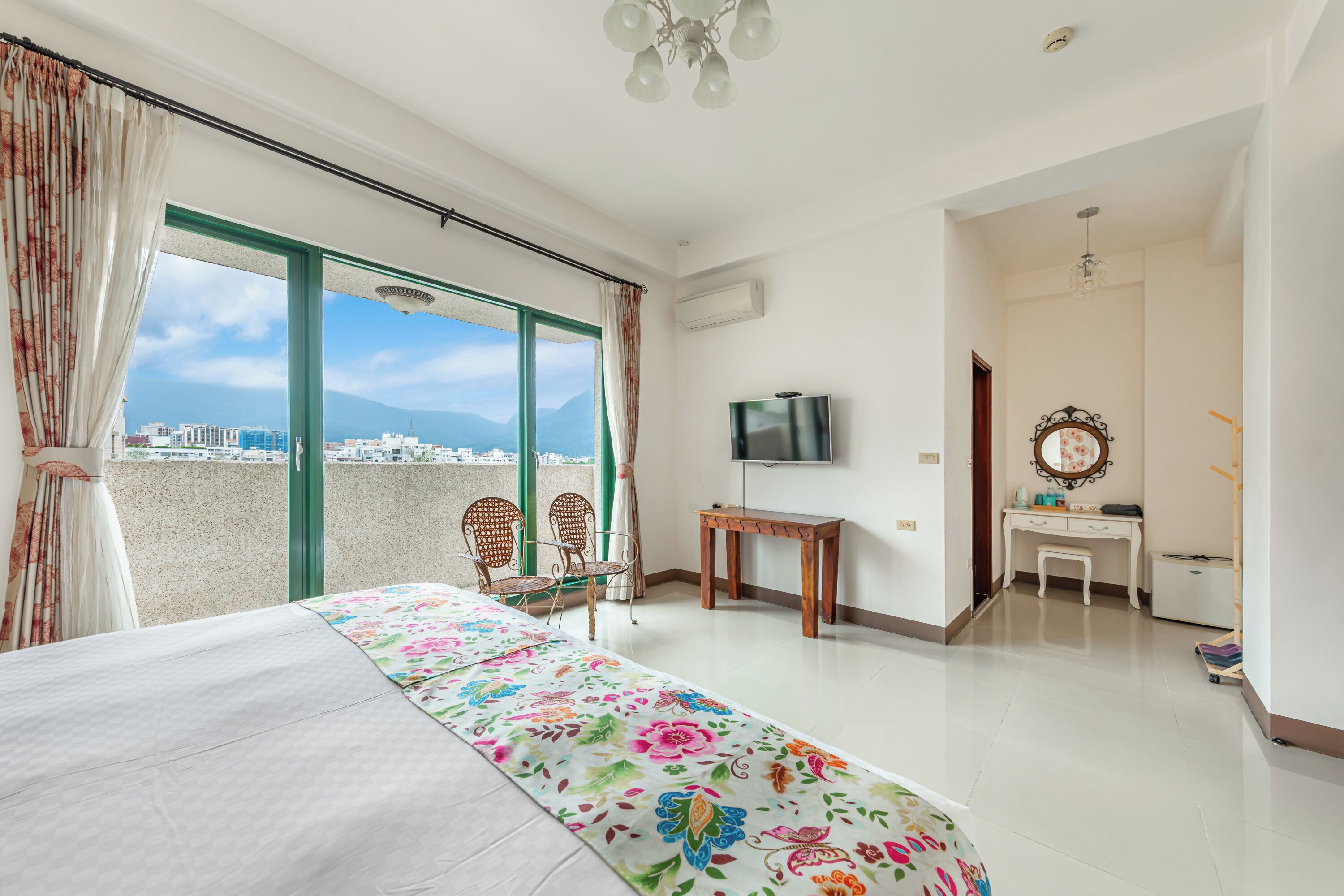 A hotel room with a balcony, a bed, a desk, a TV, and a mirror.