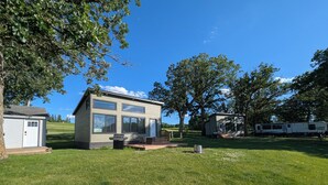 Une cabane moderne à deux étages, dotée de grandes fenêtres, d’une terrasse et d’un espace barbecue.
