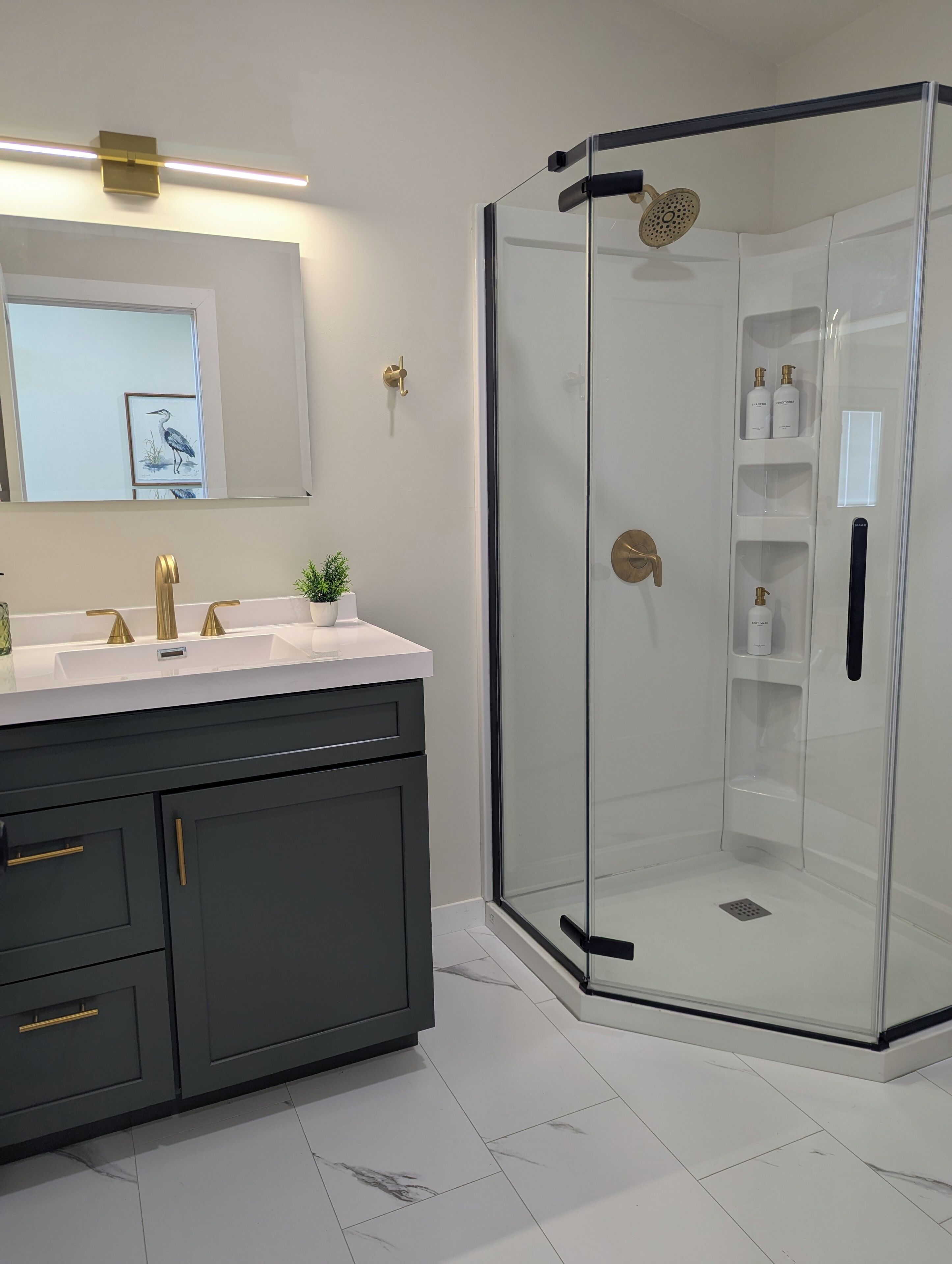 A modern bathroom with a glass-enclosed shower, a vanity with a gold faucet, and a potted plant on the counter.