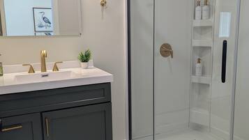 A modern bathroom with a glass-enclosed shower, a vanity with a gold faucet, and a potted plant on the counter.