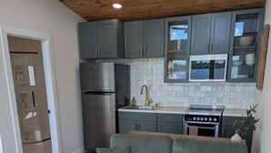 Une cuisine moderne avec des meubles gris, des appareils en acier inoxydable et un plafond en bois.