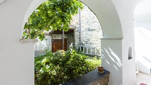 A stone building with a wooden door, surrounded by greenery and a white archway. - Typical Ligurian house with garden and sea view terrace (Cipressa)