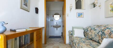 Una habitación acogedora con un escritorio de madera, un sofá floral y un baño con lavamanos y espejo.