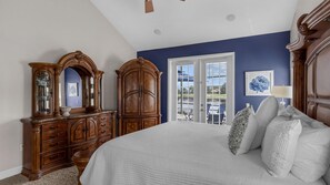 A bedroom with a large bed, wooden dresser, and a window with blinds.