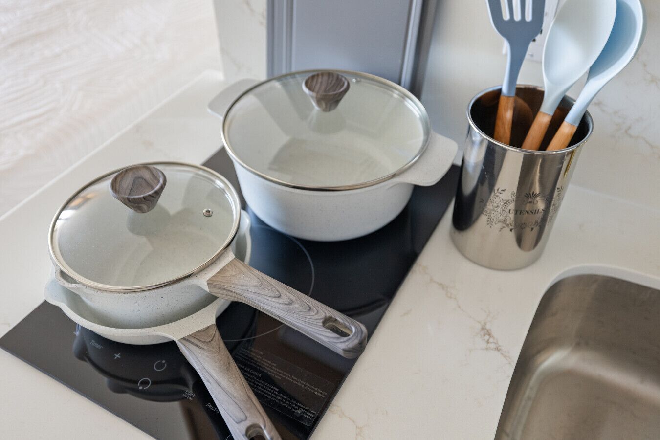 Een keuken met twee pannen op een inductiekookplaat, een roestvrijstalen pannenhouder en een spoelbak.