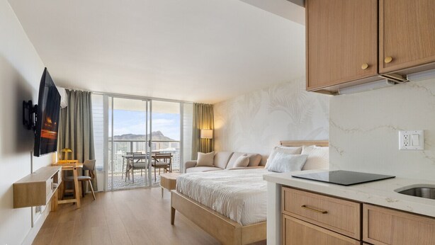 A modern hotel room with a large bed, a desk with a chair, a television, and a balcony with a view of the city. - The Palms: Waikiki studio (Honolulu)