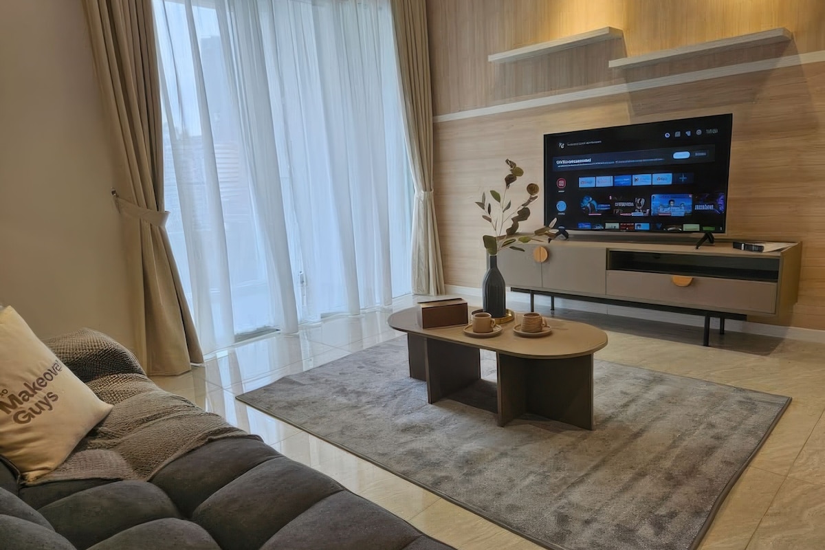 A modern living room with a sofa, a coffee table, and a flat-screen TV mounted on a wooden wall.