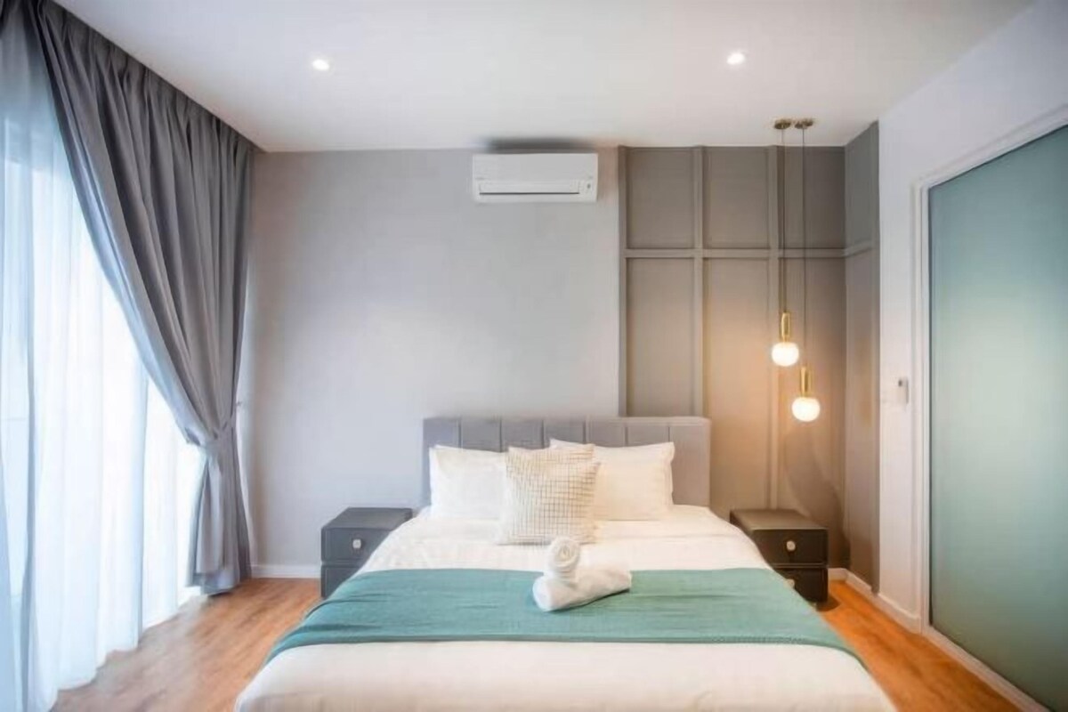 Une chambre d’hôtel moderne avec un lit bien fait, une table de chevet, une commode, un climatiseur fixé au mur et une fenêtre avec des rideaux.