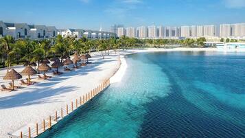 A beach resort with a white sandy shore, clear blue water, and a row of palm trees.