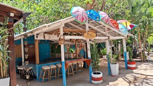 A rustic outdoor seating area with wooden tables and chairs, surrounded by potted plants and umbrellas. - CortLang Vacation Rentals Costambar (Puerto Plata)