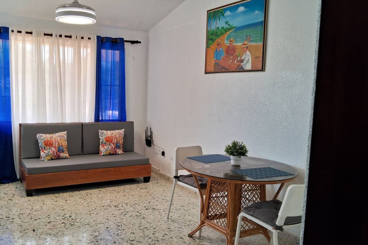 A room with a sofa, a dining table, and a painting on the wall.