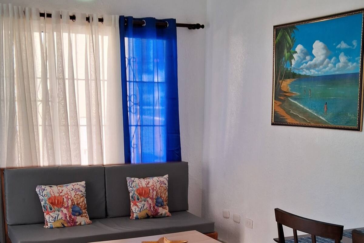 A living room with a sofa, a coffee table, a chair, a painting, and a ceiling fan.