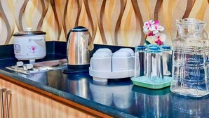 A kitchen counter with a rice cooker, a kettle, a water dispenser, and a glass bottle.