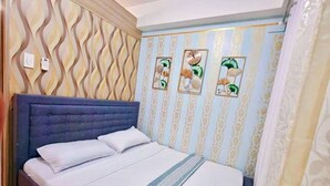 A bedroom with a tufted headboard, a bed with white linens, decorative wall panels, and a floral artwork.