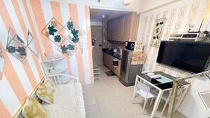 A modern kitchen with a refrigerator, microwave, and stove. There is a dining area with a white table and chairs. The room has striped walls and a fluffy white rug.