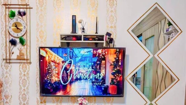 A dining area with a TV displaying a Christmas scene, a clock, and a decorative mirror.