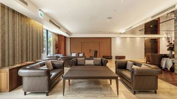 A spacious lobby with leather sofas, a central coffee table, and a mix of wood and brick walls.