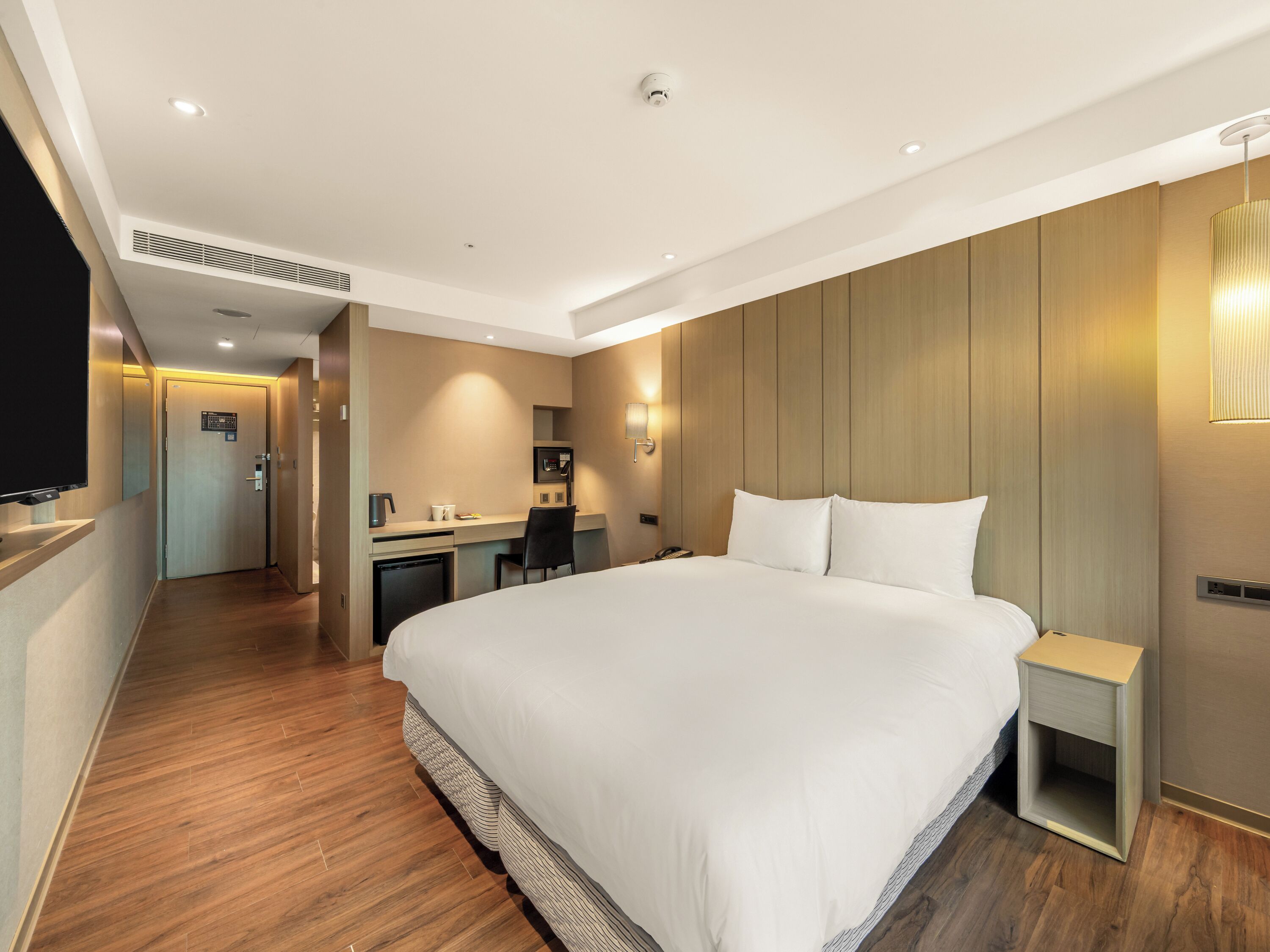 Une chambre d’hôtel avec un grand lit, un bureau, une chaise, une télévision et une petite table de chevet.