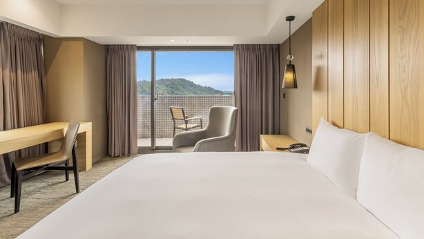 A hotel room with a large bed, a desk, a chair, and a view of a mountainous landscape through a sliding glass door. - CHECK inn SELECT - Taipei NeiHu (Taipei)
