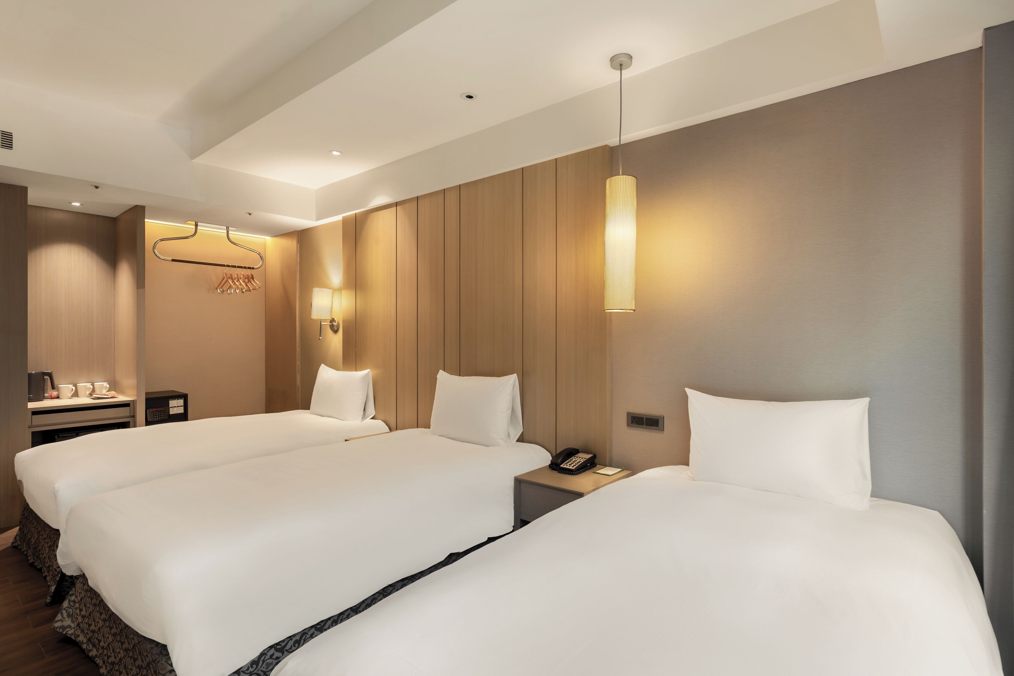 Una habitación de hotel con dos camas, mesitas de noche, una lámpara, un teléfono y un perchero.