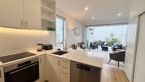 Una cucina moderna con mobili bianchi, forno integrato e lavastoviglie. C'è un'area pranzo con divano e sedie, e un'ampia finestra che offre luce naturale.