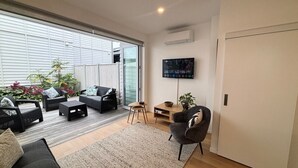 Un soggiorno moderno con un'ampia porta-finestra scorrevole che dà su un balcone, arredato con un divano, un tavolino da caffè e una TV a parete.
