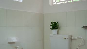Een compacte, schone badkamer met toilet, douche en een plant in een pot op de muur.
