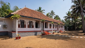 A two-story house with a tiled roof, a porch with potted plants, and a stone foundation. - Kuttanad Kayak Club- Riverside Heritage Homestay In Alleppey Backwater village (Alappuzha)