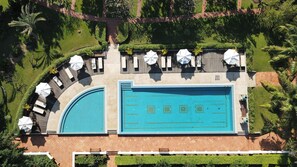 Vista aérea de un resort con una amplia piscina rectangular, tumbonas y un jardín bien cuidado.