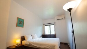 Une chambre d’hôtel comprenant un lit, une table de chevet, une lampe, un appareil de climatisation et une fenêtre avec des rideaux.